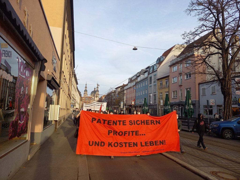 Frontblock der 5. lockdown capitalism Demo in Würzburg am 20.02.2021. Auf dem Fronttranspi der Gruppe Klein-Nizza steht schwarz auf rot: "Patente sichern Profite... und kosten Leben!"